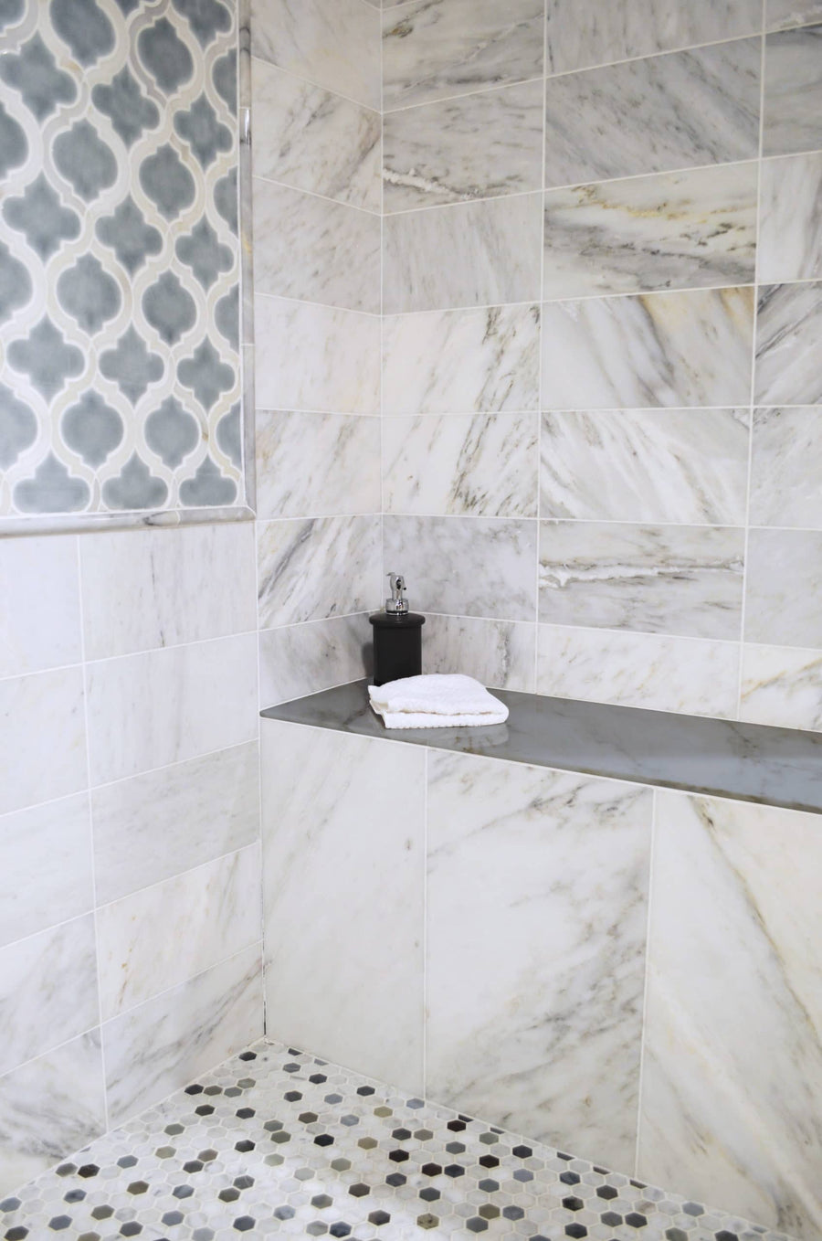 A modern shower features large white and gray marble tiles, a gray countertop with folded towels, black soap dispenser, hexagonal floor tiles, and 16x48 Shower Bench Top for stylish and comfortable seating.