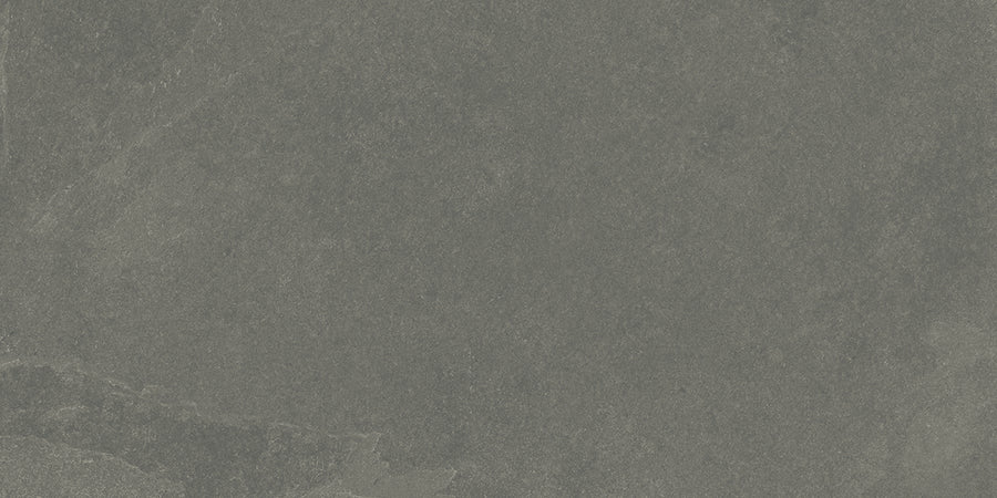 A close-up view of the Shyft 12x24 Rectified Porcelain Tile reveals a textured, dark gray stone look with subtle color variations and natural veining, reminiscent of Brazilian slate.