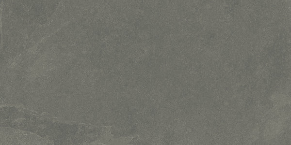 A close-up view of the Shyft 12x24 Rectified Porcelain Tile reveals a textured, dark gray stone look with subtle color variations and natural veining, reminiscent of Brazilian slate.