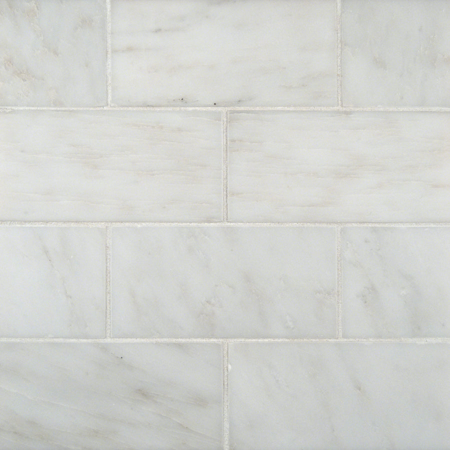 Close-up of Arabescata Carrara Select 3x6 Marble tiles arranged in a staggered brick pattern. These natural stone tiles have white and gray tones with subtle gray veining and visible grout lines.