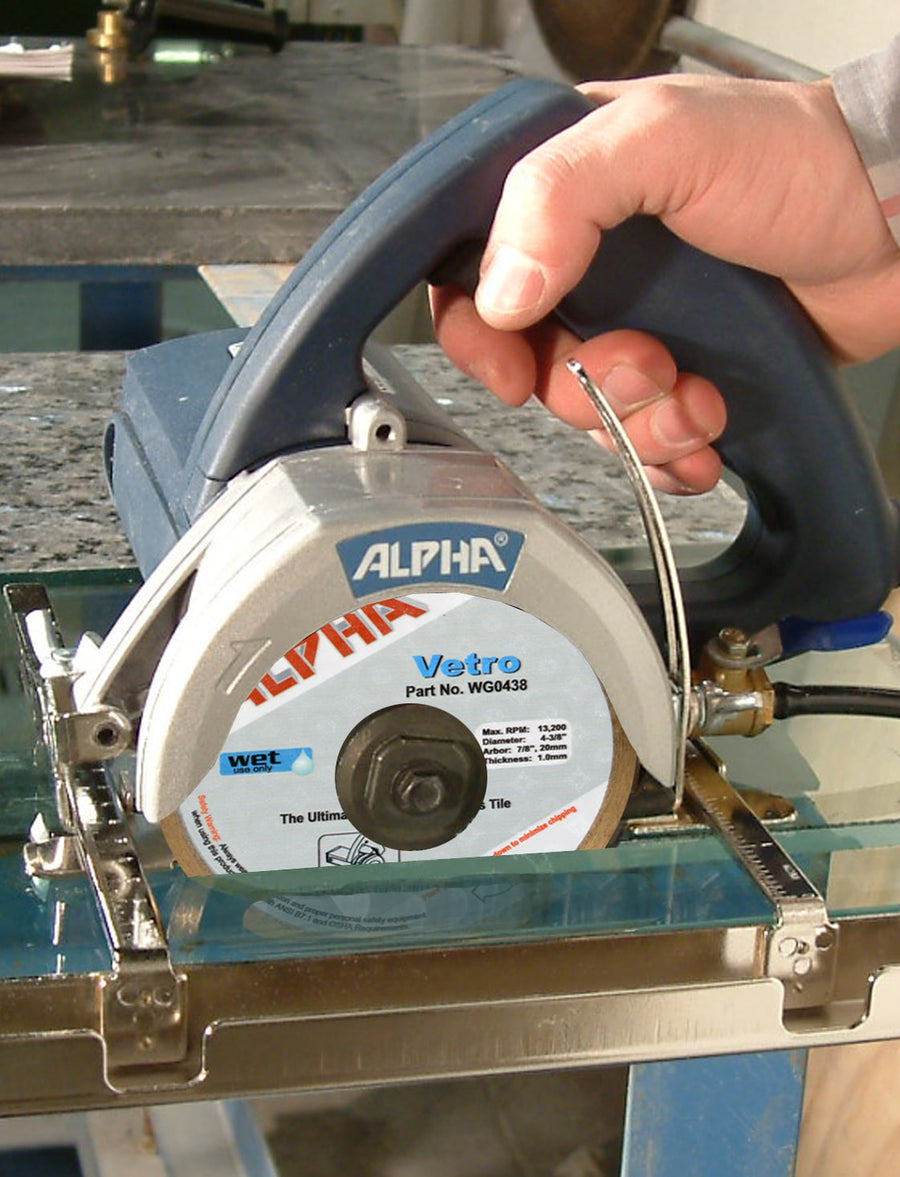 A hand uses the Alpha Vetro Wet Blade for Glass on a wet saw to achieve chip-free cutting through a glass tile secured on a work surface.