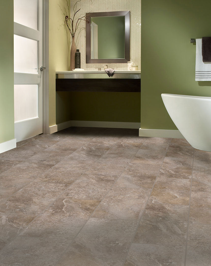 Modern bathroom with green walls, Corinthian Coast Adura® Max 12x24 Vinyl Tile flooring, white freestanding bathtub, towel rack, floating dark wood vanity with mirror above, decorative branches in a vase, and natural light through a frosted door.