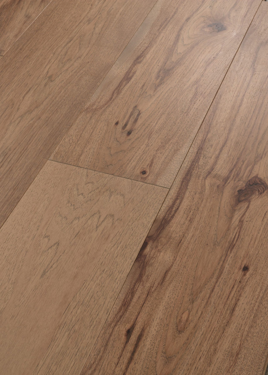 Close-up of Vogue 9 1/4" Hickory & Red Oak Hardwood flooring with a light brown finish, visible wood grain and knots. Neatly aligned planks showcase the smooth texture and rich color variations.