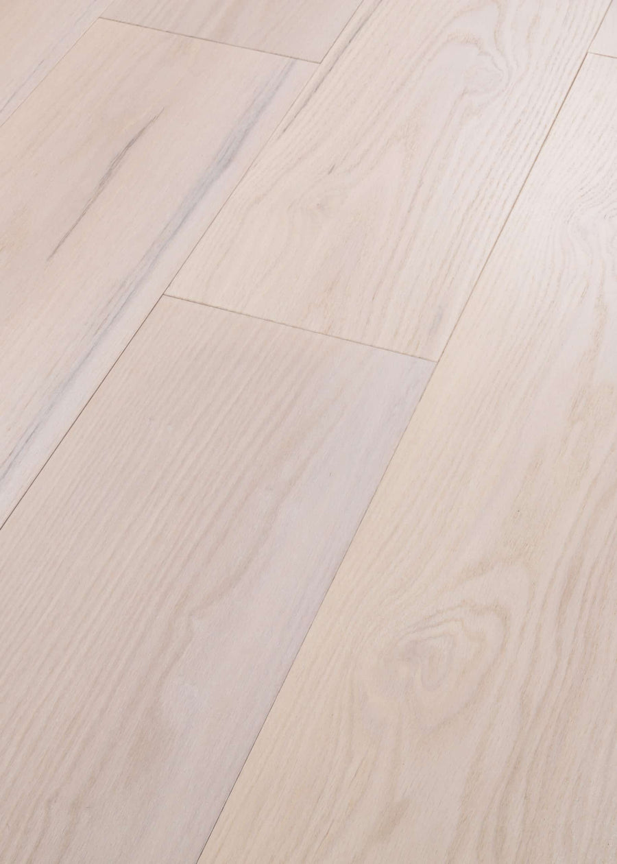 Close-up of Vogue 9 1/4" Hickory & Red Oak Hardwood floors featuring splash-proof, smooth-finish planks with subtle wood grain patterns and visible seams between each light-toned board.