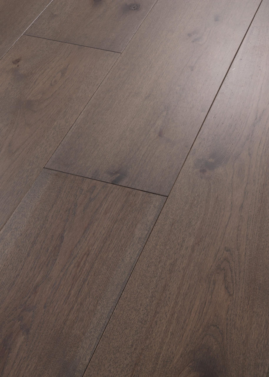 Close-up of Vogue 9 1/4" Hickory & Red Oak Hardwood featuring dark brown planks with visible grain patterns and knots, a smooth matte finish, and a staggered layout.