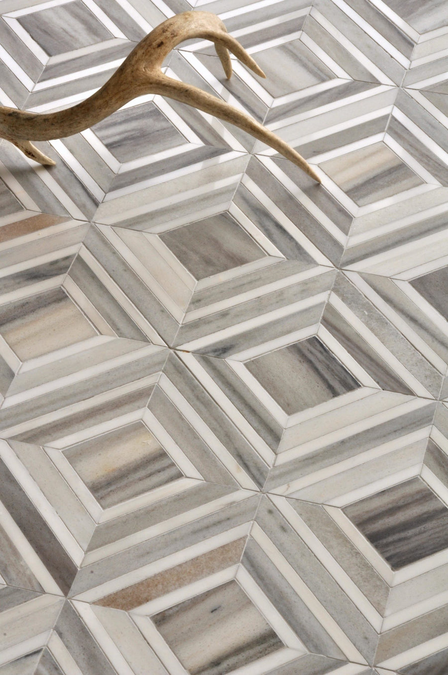 The Talya Yildiz 8 13/16 x 11 Waterjet Natural Stone tile features a gray and white three-dimensional cube pattern floor, evoking modern geometry, with a light brown antler displayed in the upper left corner.