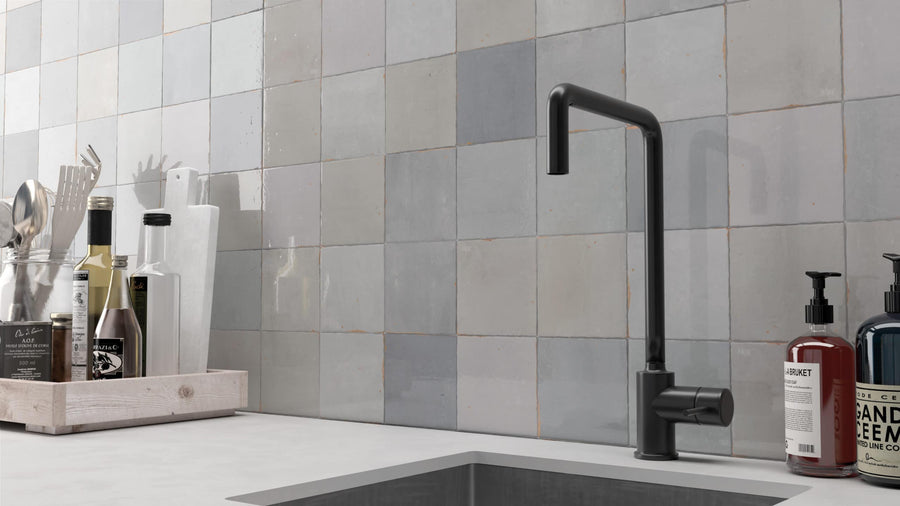 A modern kitchen sink with a matte black faucet, a backsplash of Zellige 5x5 Glossy Subway Tile in gray, and countertop items including utensils in a holder, cutting boards, and soap dispensers.