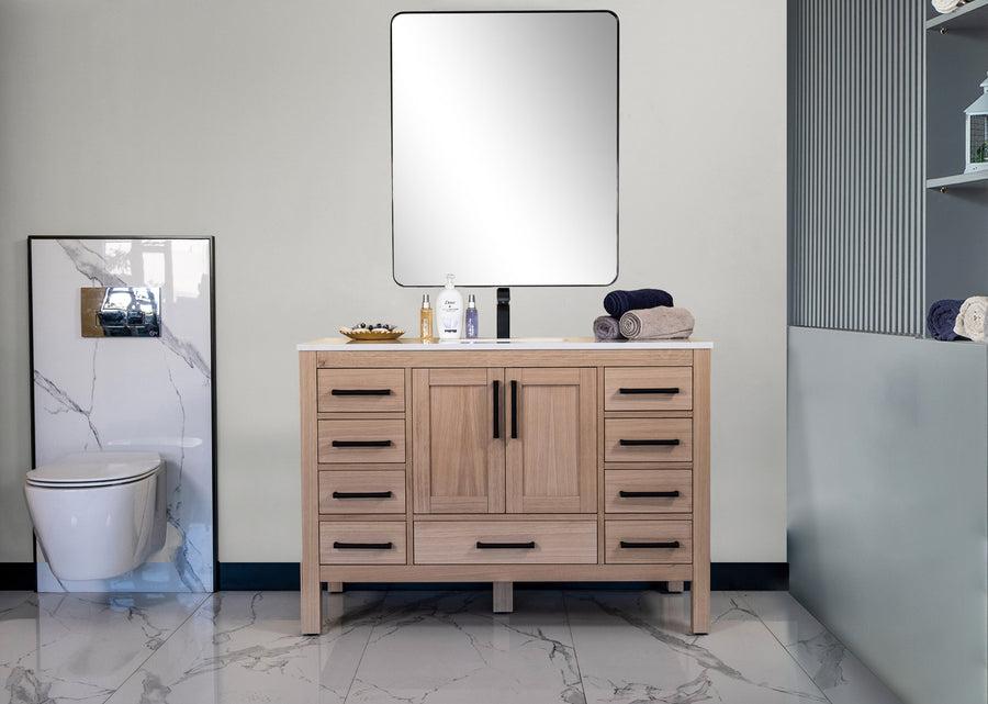 Modern bathroom with Ashley 48" Vanity in natural oak and black handles, square mirror above, marble-finished floor and walls, toiletries on the countertop, towels stacked on shelves, and toilet to the left.