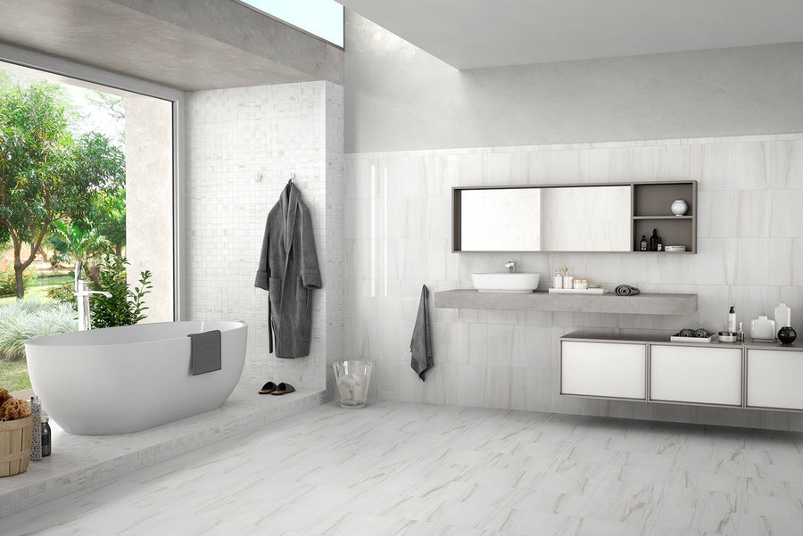 Modern white bathroom with Ontario 13x26 Porcelain Tile flooring, a large soaking tub, wall-mounted sink and shelves, hanging gray robe, toiletries, and a large window that fills the space with natural light and views of green trees.