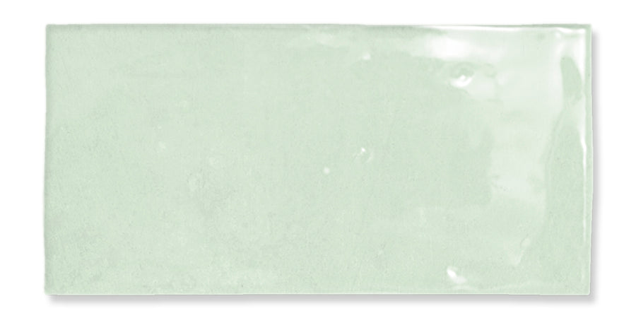 The Fez 2.5x5 Subway Tile is a rectangular, glossy, light green glazed ceramic tile with a smooth surface and subtly uneven edges, inspired by traditional Zellige craftsmanship, shown on a white background.