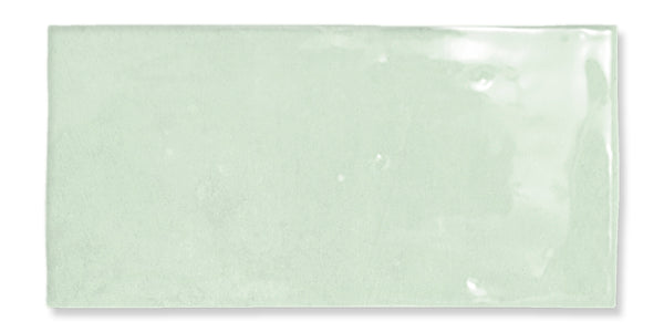 The Fez 2.5x5 Subway Tile is a rectangular, glossy, light green glazed ceramic tile with a smooth surface and subtly uneven edges, inspired by traditional Zellige craftsmanship, shown on a white background.